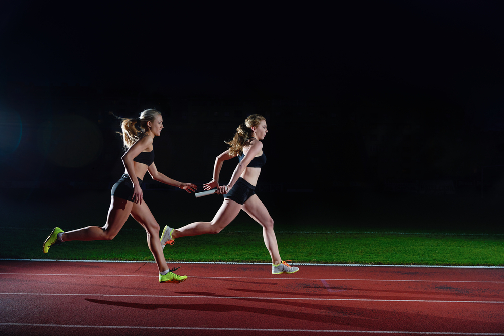 woman athletic runners passing baton in relay race